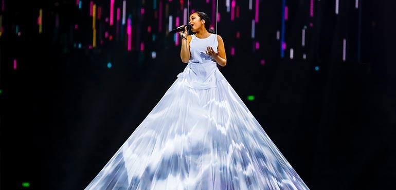 Girl sings into a microphone as she is lifted upwards.